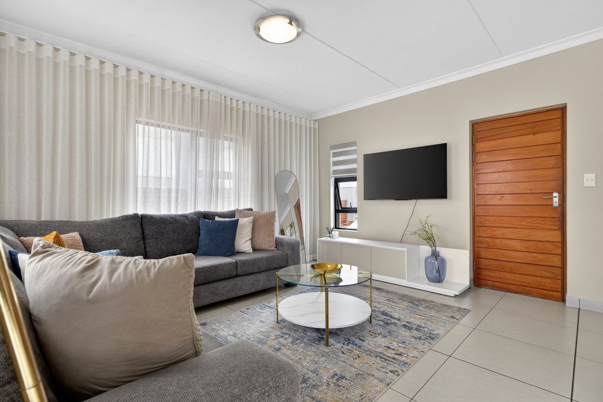 A well-maintained living room featuring neutral tiled flooring, a modern flush mount ceiling light, and a solid timber door.
