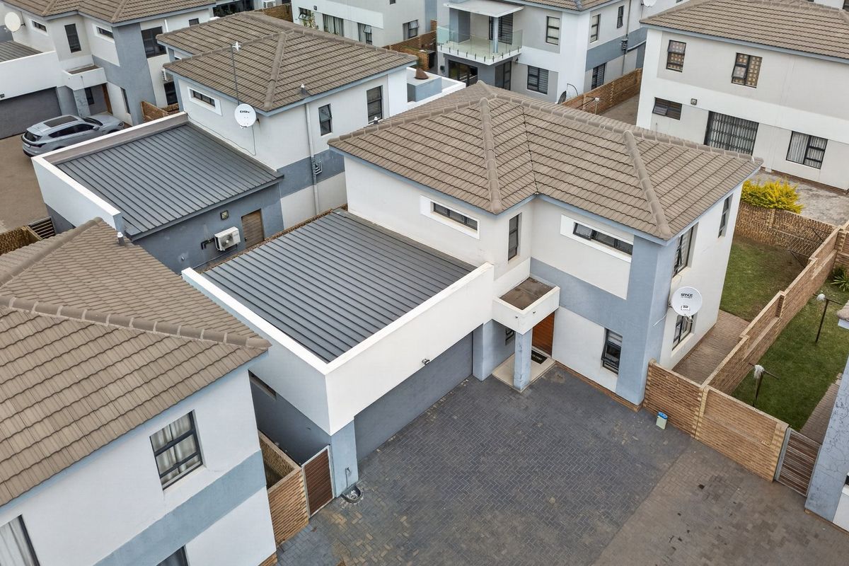 An aerial view of a modern residential property featuring a tiled roof, paved driveway, and attached garage within a suburban estate setting.