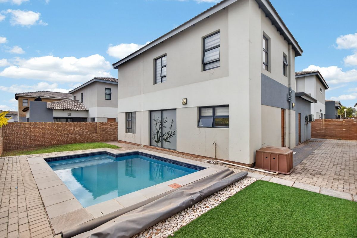 Rear exterior view of a modern two-story house featuring a private swimming pool, paved patio area, and enclosed garden with brick boundary walls.