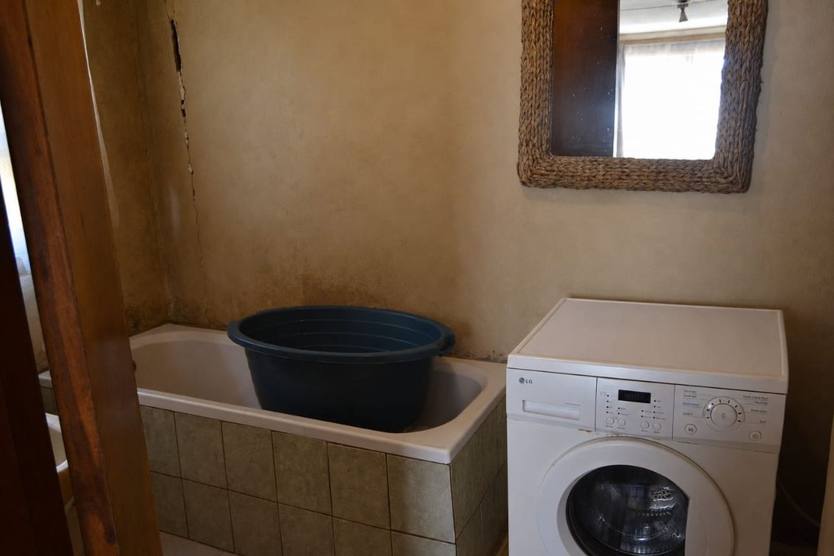 A dated bathroom featuring a bathtub with tiled surround and a built-in washing machine, showing signs of wall damage and wear.