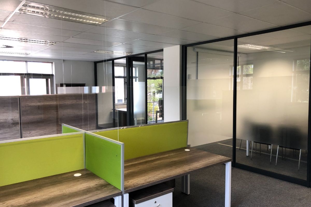 Modern commercial office space featuring glass partition walls, suspended ceilings with recessed lighting, and carpeted flooring.