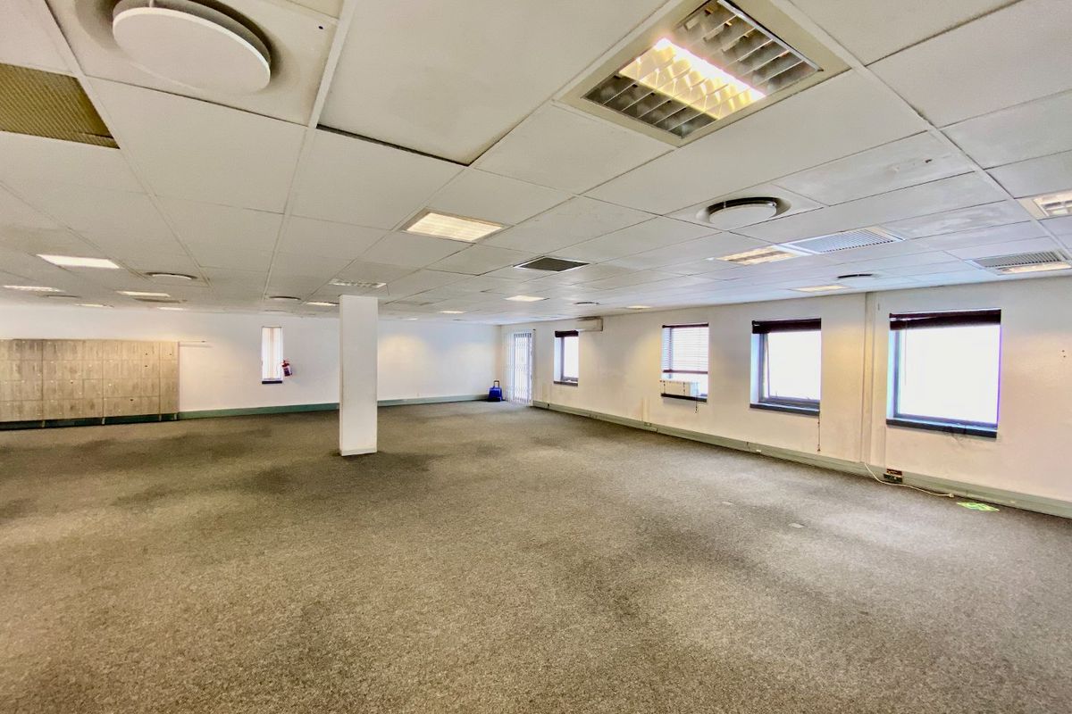Spacious open-plan commercial office area featuring suspended ceilings, recessed lighting, carpeted flooring, and built-in storage lockers.