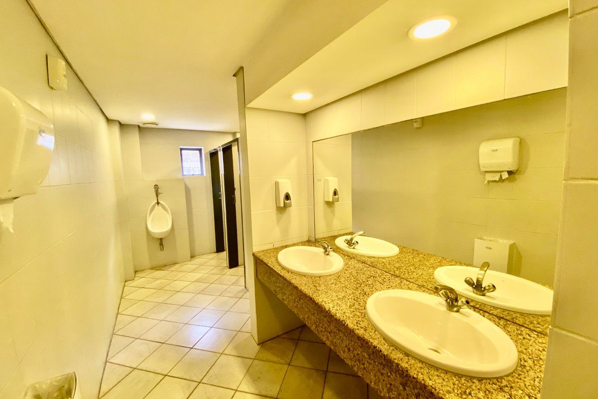 Commercial bathroom facility featuring dual vanity basins with granite countertop, wall-to-wall mirror, tiled flooring, and a separate urinal area.