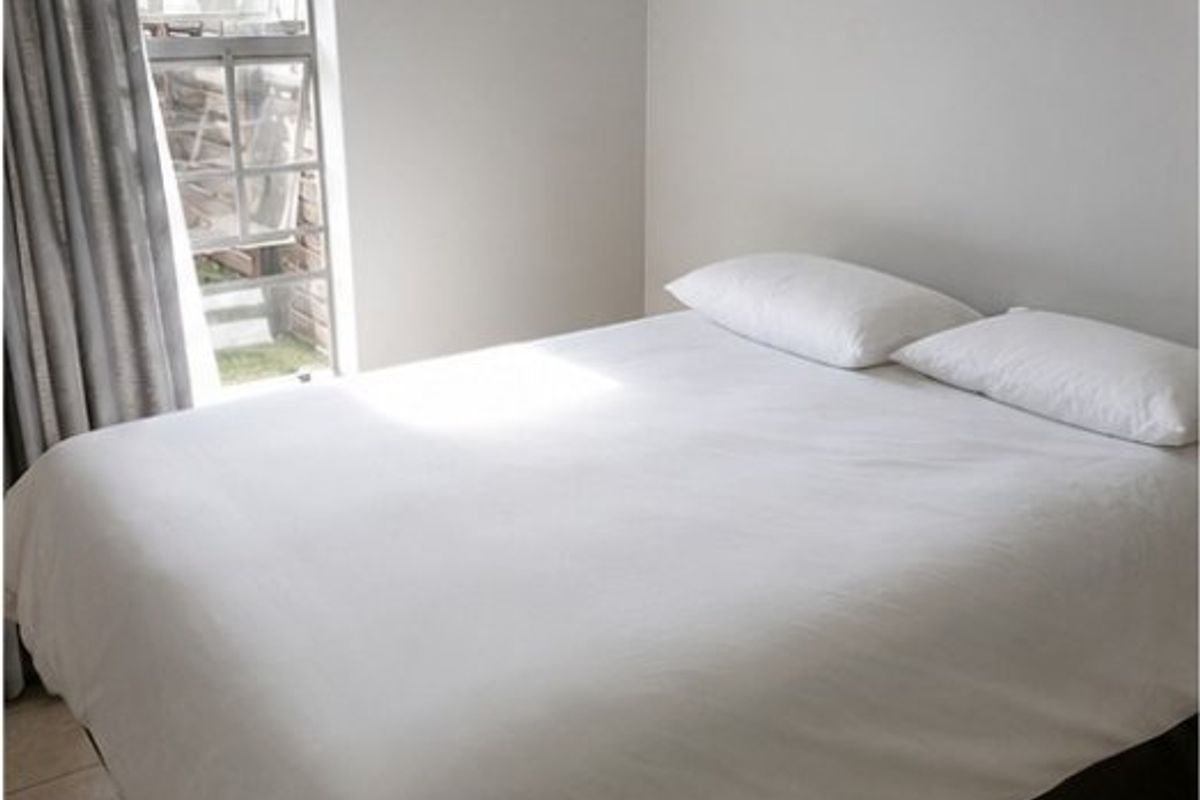 A simple bedroom featuring tiled flooring and a window with security bars, providing a functional and neutral living space.