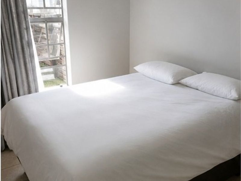 A simple bedroom featuring tiled flooring and a window with security bars, providing a functional and neutral living space.