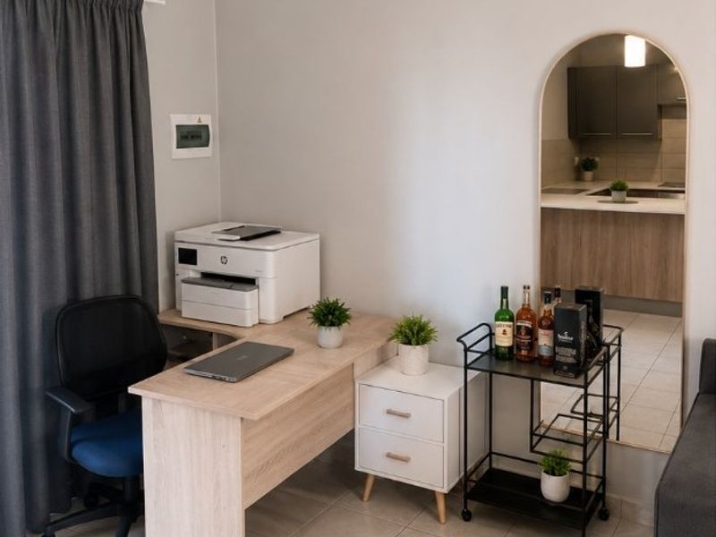 A functional home office space featuring tiled flooring and a decorative archway providing a view into the adjacent kitchen area.