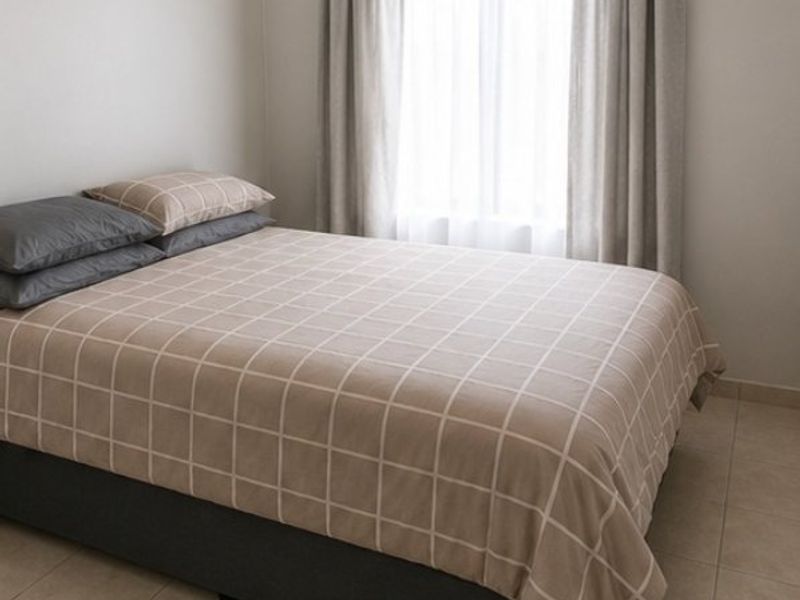 A simple bedroom featuring neutral wall tones, tiled flooring, and a window dressed with curtains.