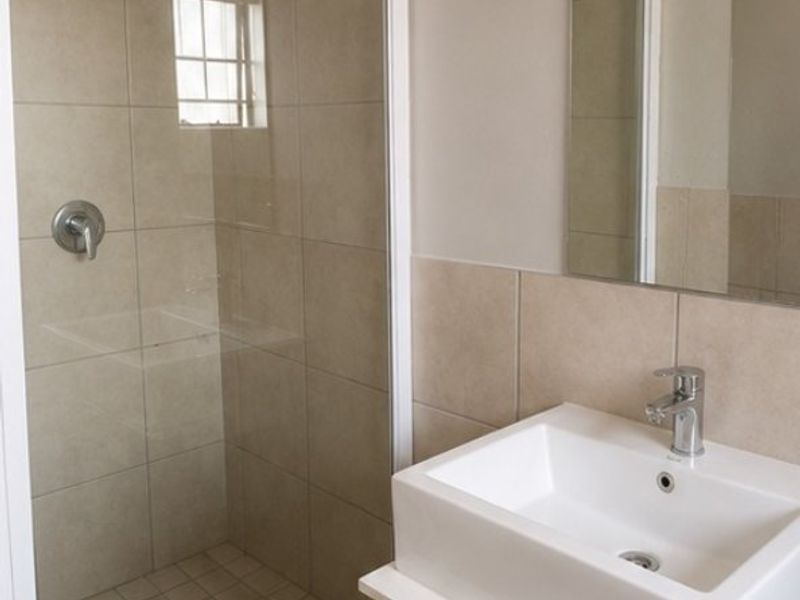 A clean, modern bathroom featuring a glass-enclosed shower, a contemporary vanity basin with storage cabinet, and neutral wall tiling.