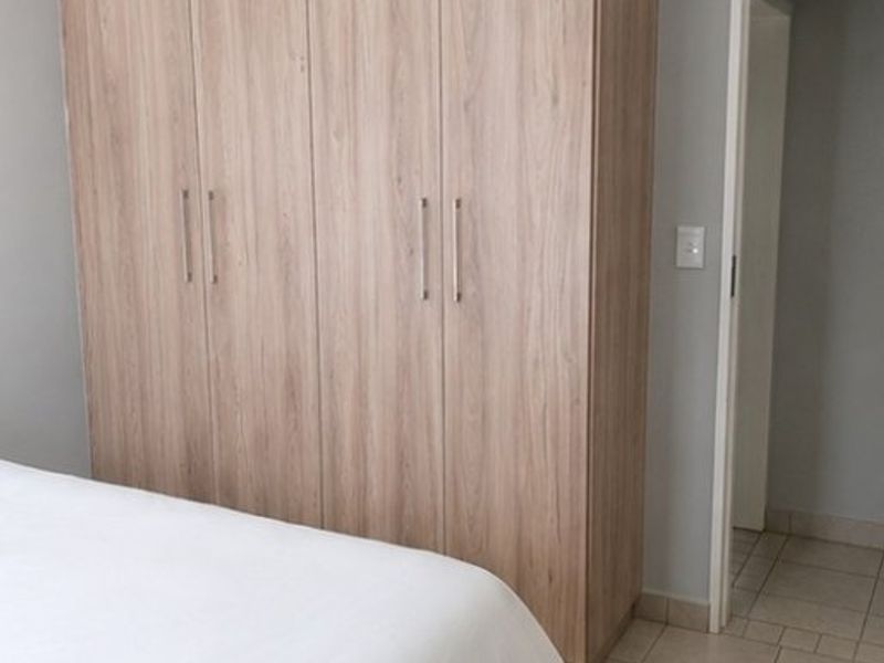 A bedroom featuring a modern wood-finish built-in wardrobe and neutral tiled flooring, providing clean and functional storage space.