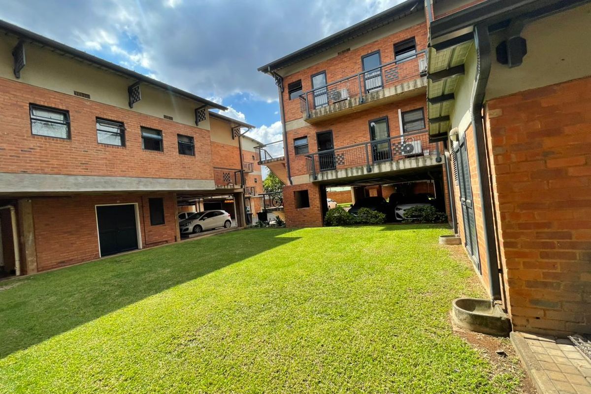 A view of the rear courtyard area featuring brick apartment buildings, balconies, and a central lawn with covered parking bays.