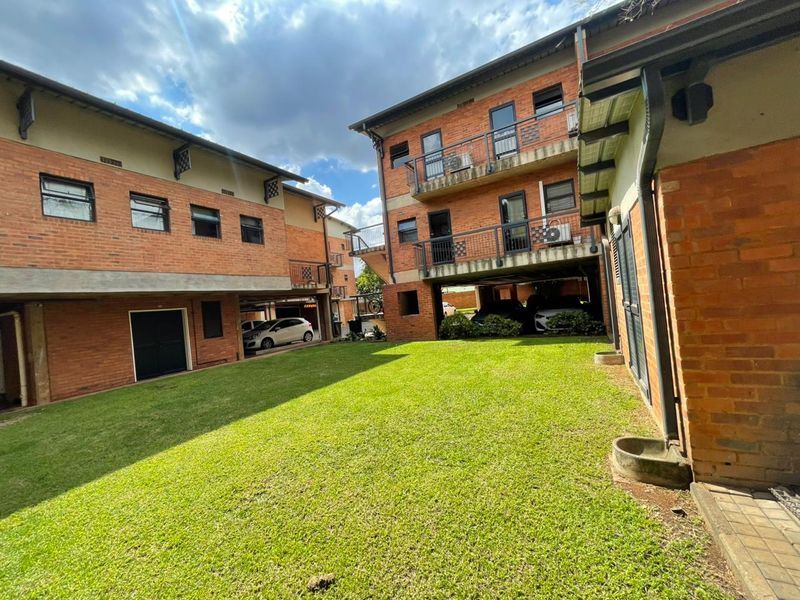 A view of the rear courtyard area featuring brick apartment buildings, balconies, and a central lawn with covered parking bays.