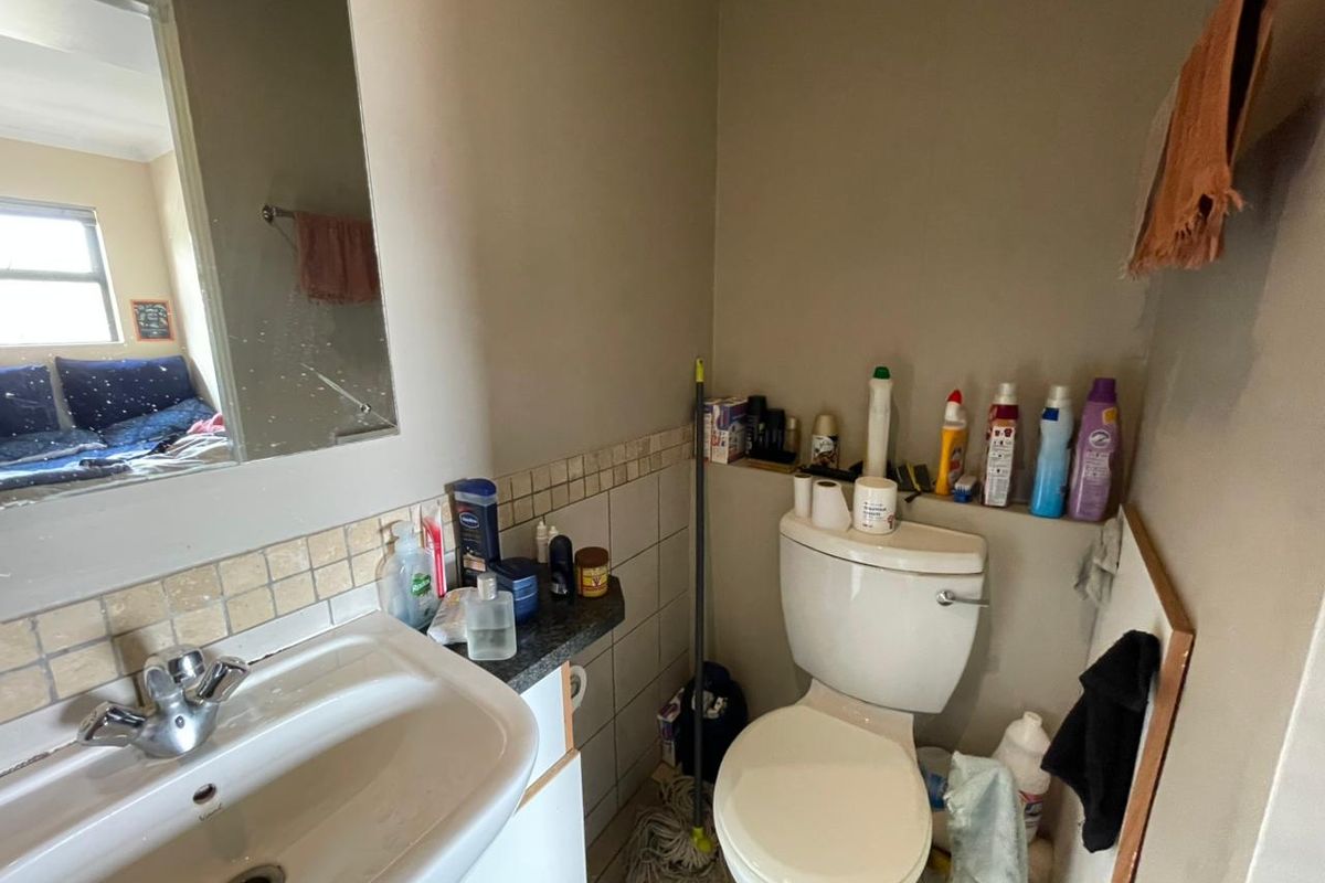 A compact bathroom featuring a ceramic basin with chrome mixer tap, wall-mounted mirror, and standard toilet with tiled splashback finishes.