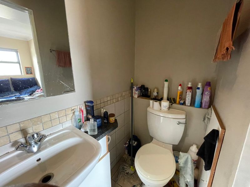 A compact bathroom featuring a ceramic basin with chrome mixer tap, wall-mounted mirror, and standard toilet with tiled splashback finishes.