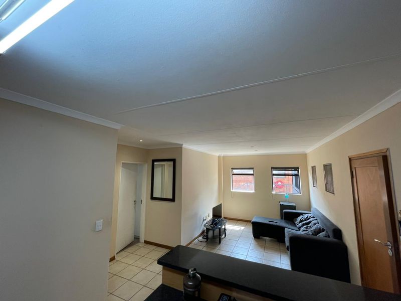 Open plan living area featuring tiled flooring, a breakfast bar, and coved ceilings, providing a functional space with natural light from dual windows.