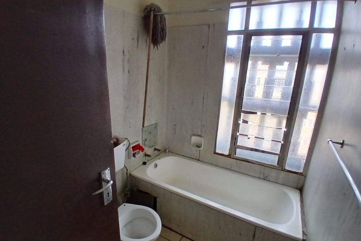 A dated bathroom featuring a standard bathtub, toilet, and tiled flooring, requiring significant cosmetic updates and refurbishment to improve its condition.