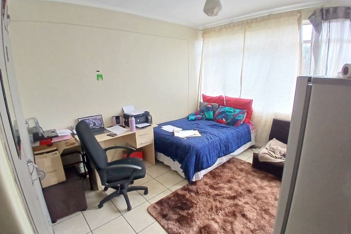 A functional bedroom featuring tiled flooring and a large window, providing natural light and a practical layout for living.