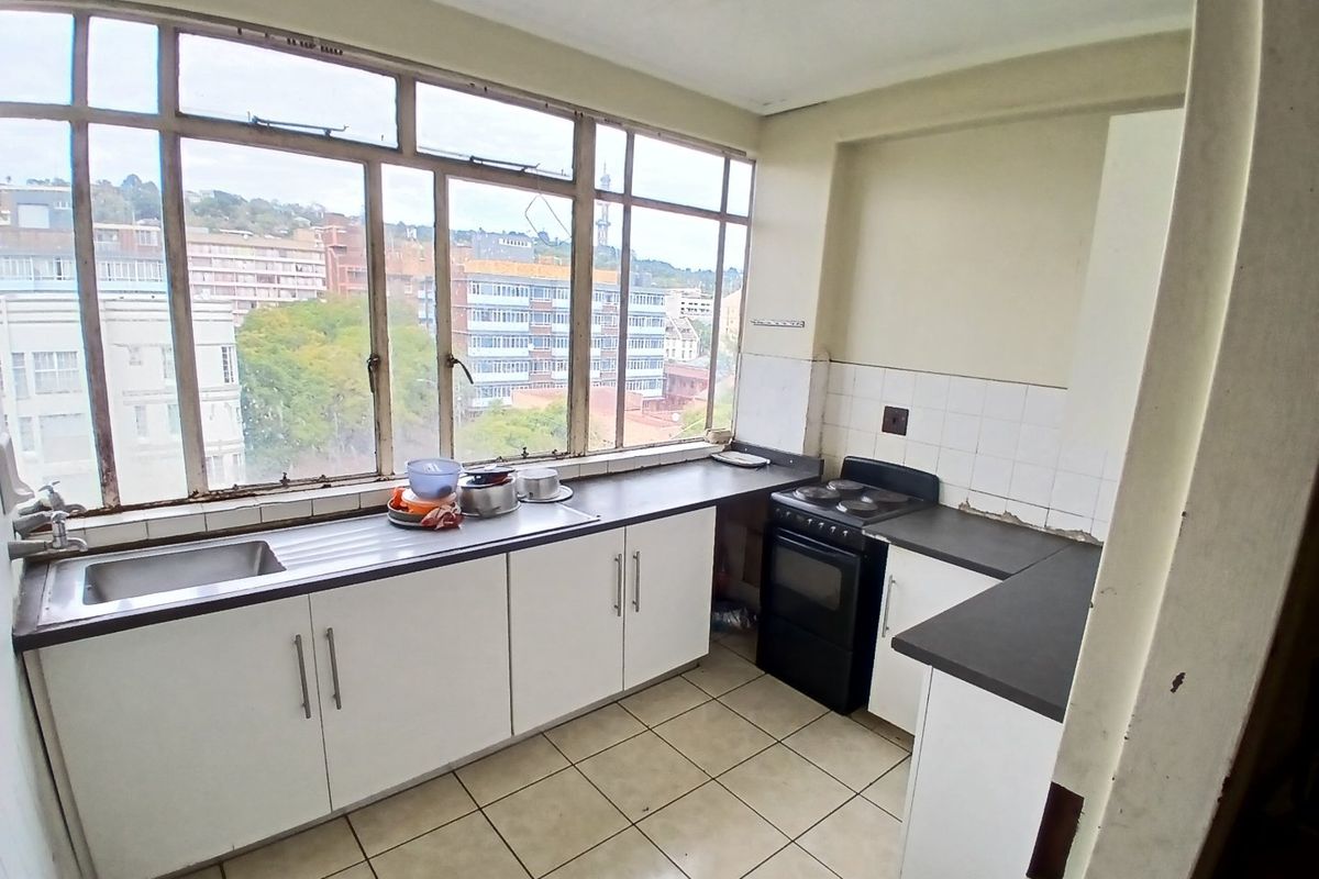 A functional kitchen featuring white cabinetry, a stainless steel sink, tiled flooring, and a large window providing natural light and urban views.