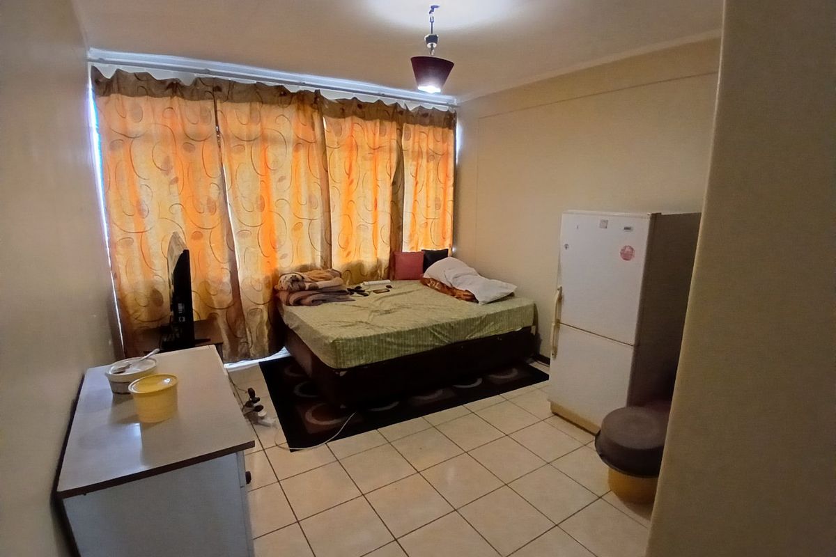 A compact bedroom featuring tiled flooring and a central pendant light fixture, currently utilized as a multi-purpose living space.