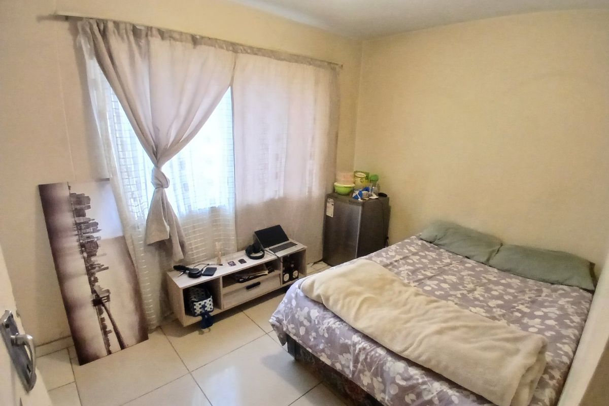 A compact bedroom featuring tiled flooring and a window with a curtain rail, providing a functional living space.