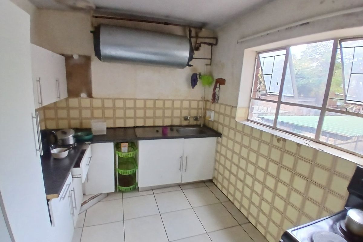 A dated kitchen featuring tiled walls and flooring, built-in cabinetry, and an exposed electric water heater, requiring significant renovation and cosmetic updates.