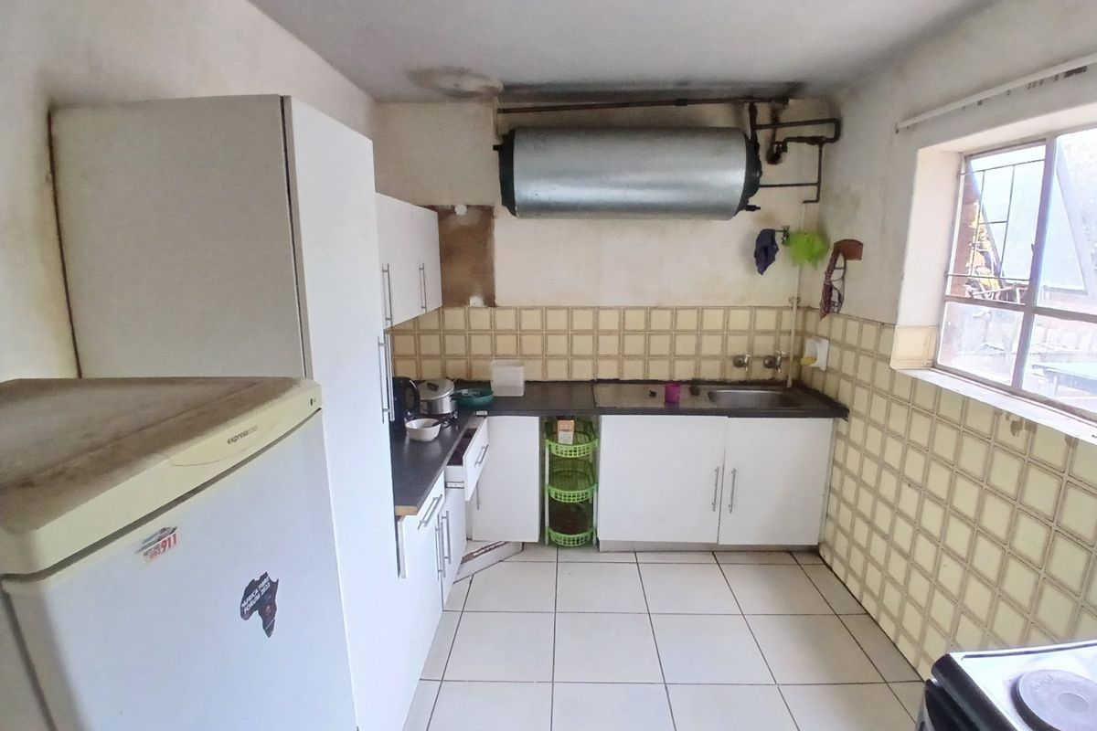 A dated kitchen featuring white cabinetry, tiled backsplash, and exposed water heater, requiring cosmetic updates and modernization of finishes.