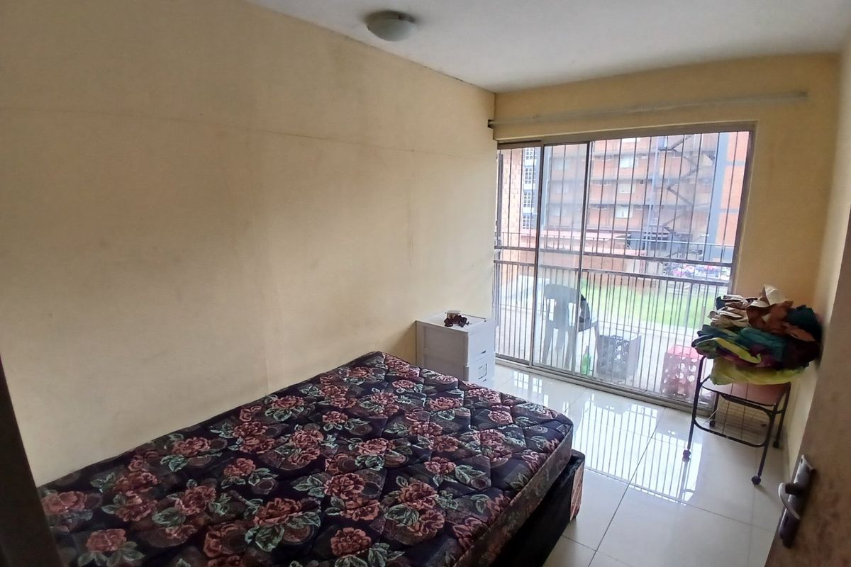A bedroom featuring tiled flooring and a sliding glass door with a security gate, providing access to an outdoor area.