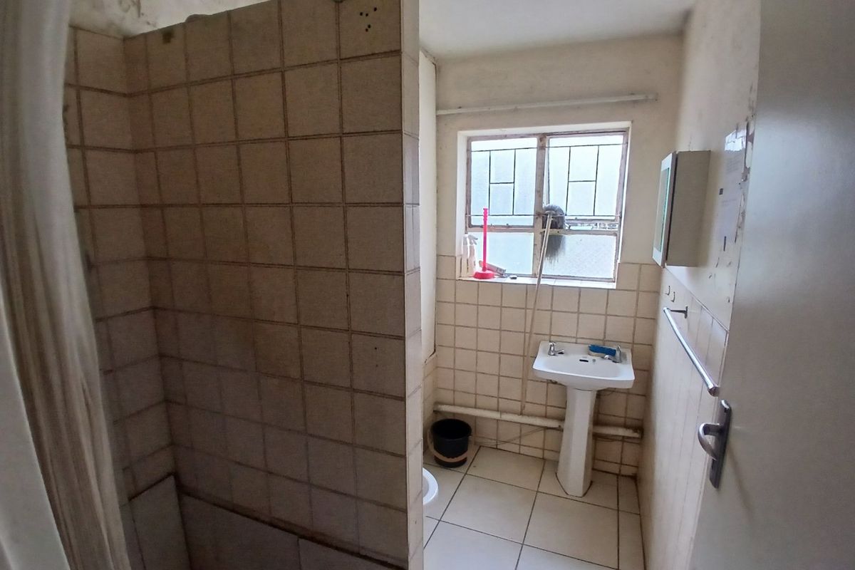 A dated bathroom featuring a tiled shower enclosure and pedestal basin, requiring renovation to update the finishes and address wall surface deterioration.