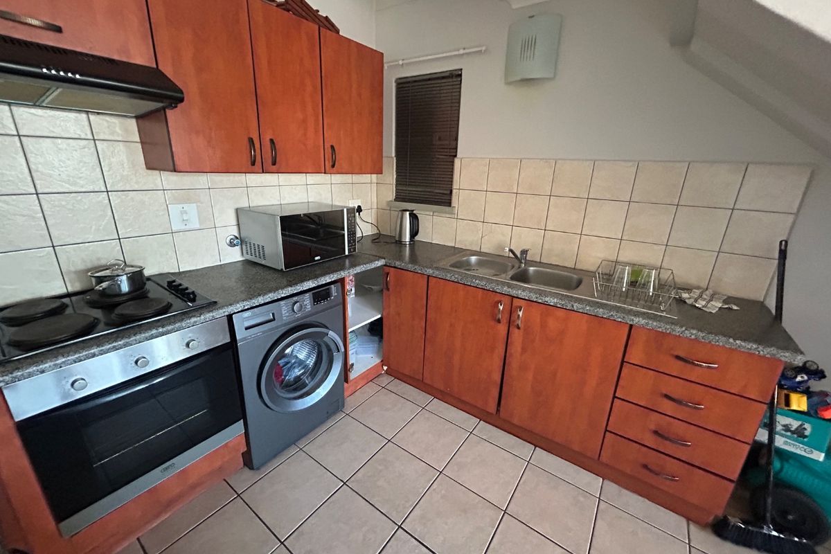 Functional kitchen featuring wood-finish cabinetry, laminate countertops, double sink, built-in oven, and hob, with tiled flooring and backsplash.