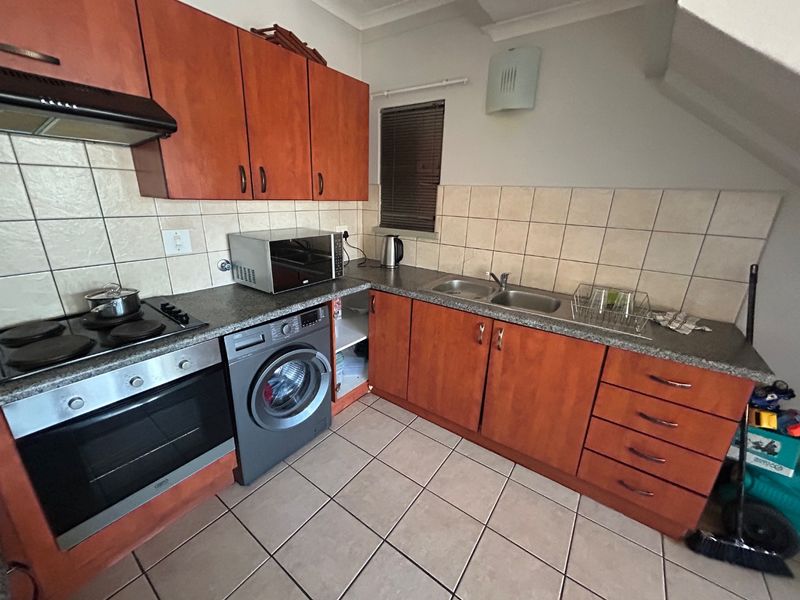 Functional kitchen featuring wood-finish cabinetry, laminate countertops, double sink, built-in oven, and hob, with tiled flooring and backsplash.
