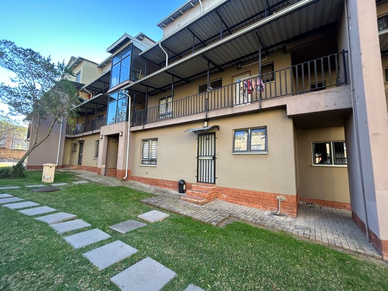 Rear elevation of a multi-story apartment complex featuring brick and plaster finishes, metal balcony railings, and paved ground-level access.
