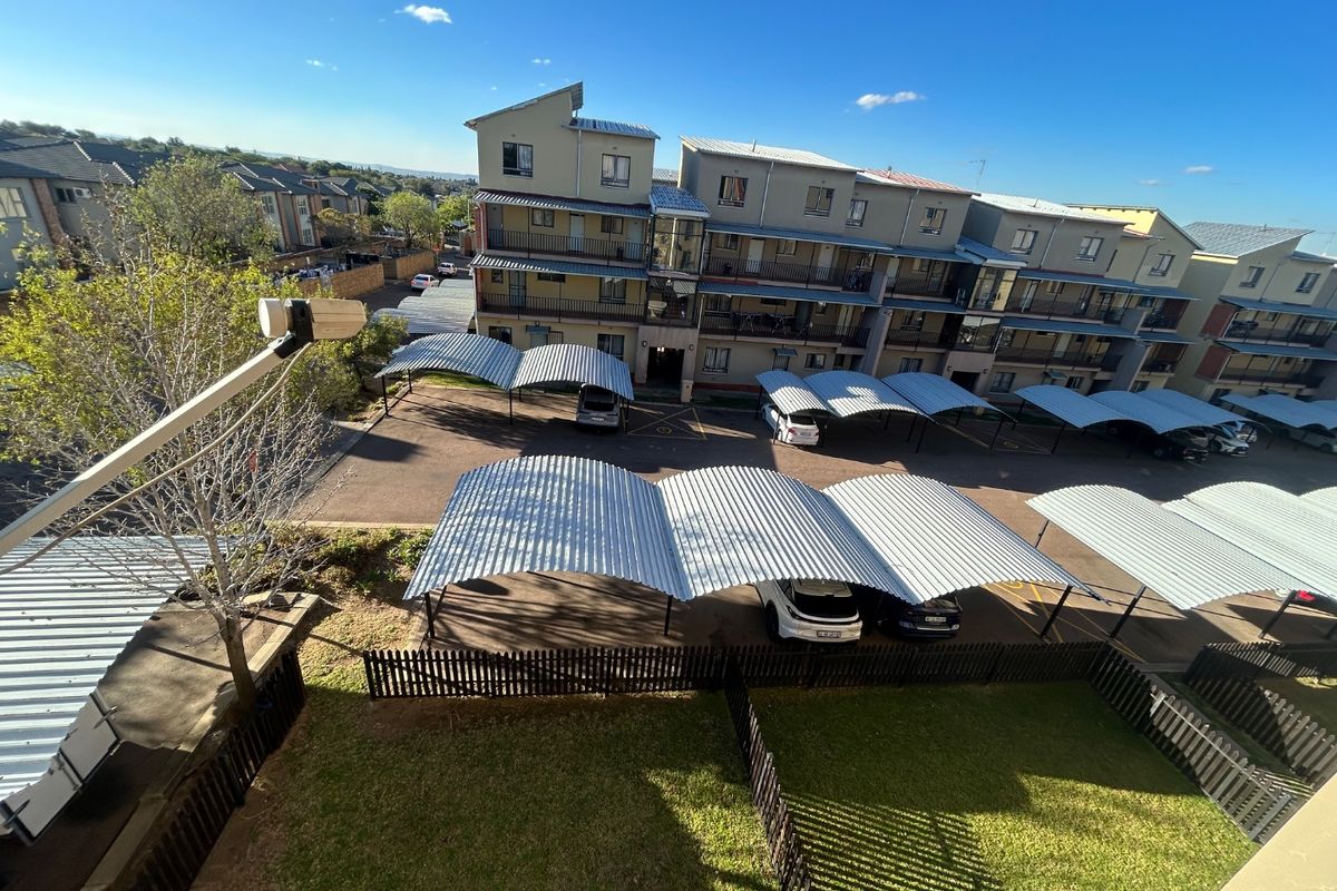 Aerial view of the apartment complex showing the building exterior, designated carport parking bays, and communal garden areas.