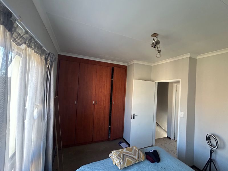 A bedroom featuring built-in wooden cupboards and neutral wall finishes, providing a functional space with direct access to the hallway.