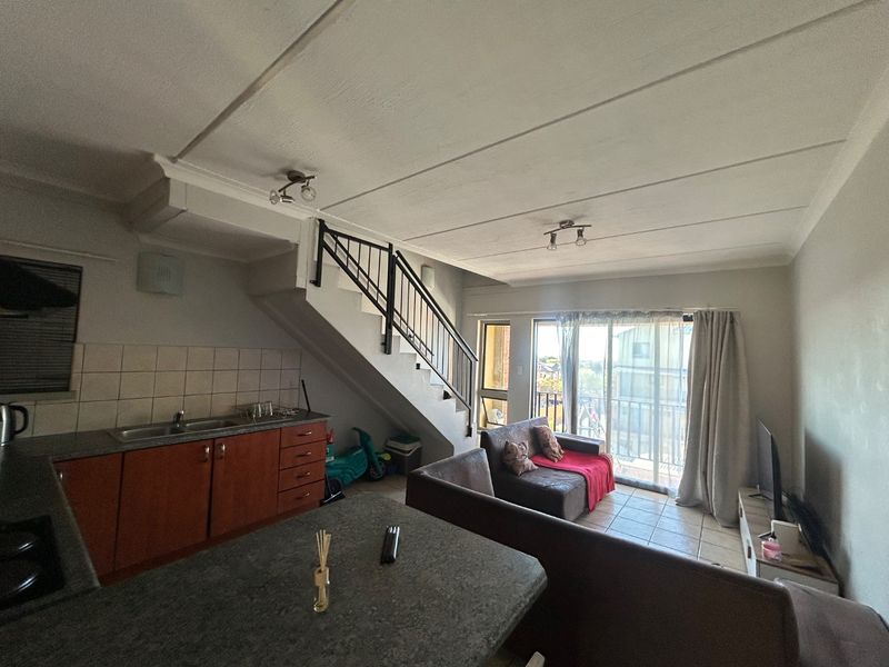 Open-plan living area featuring a compact kitchen with tiled backsplash, staircase with metal balustrade, and sliding door access to a balcony.