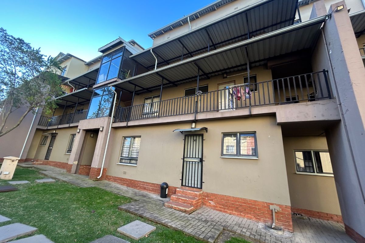 Rear elevation of a multi-story apartment complex featuring metal balconies, security gates, and paved ground-level access.