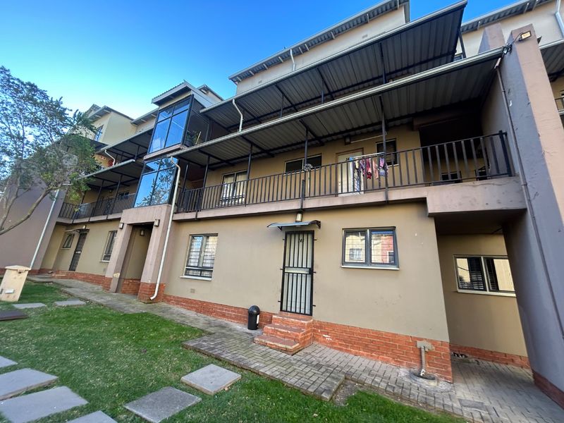 Rear elevation of a multi-story apartment complex featuring metal balconies, security gates, and paved ground-level access.