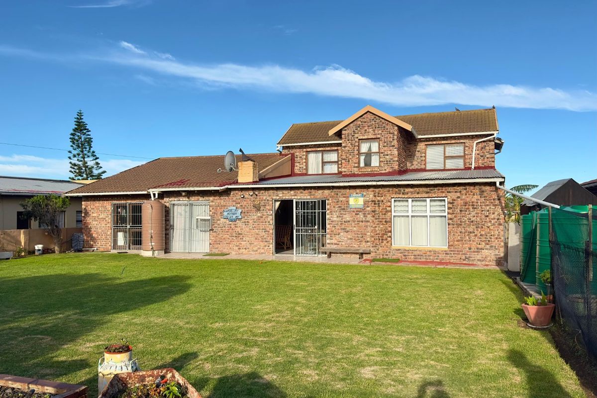 Rear view of a double-storey face brick house featuring a spacious lawn, security gates, and water storage tanks.