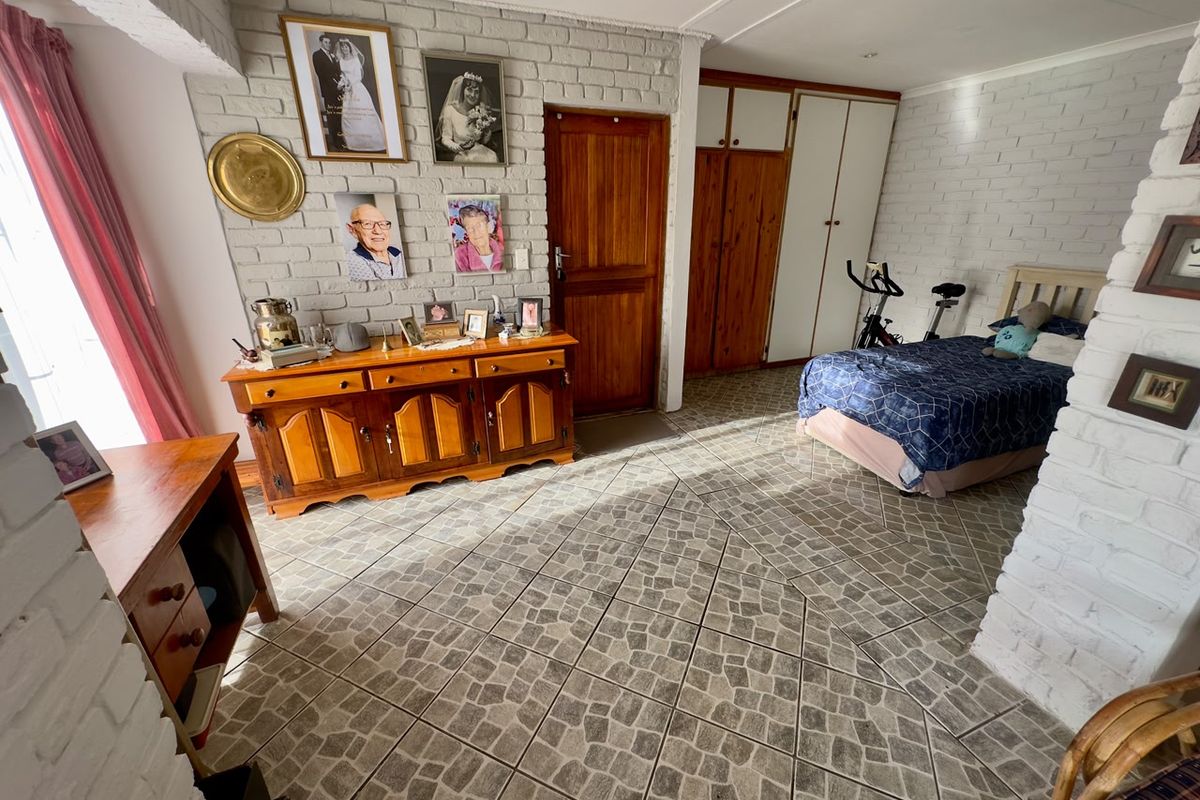 Spacious bedroom featuring painted brick walls, tiled flooring, and built-in wooden cupboards, offering a functional layout with natural light.