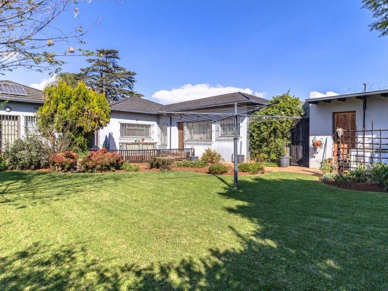 A spacious rear garden featuring a well-maintained lawn, established landscaping, and a tiled roof house with security bars on the windows.