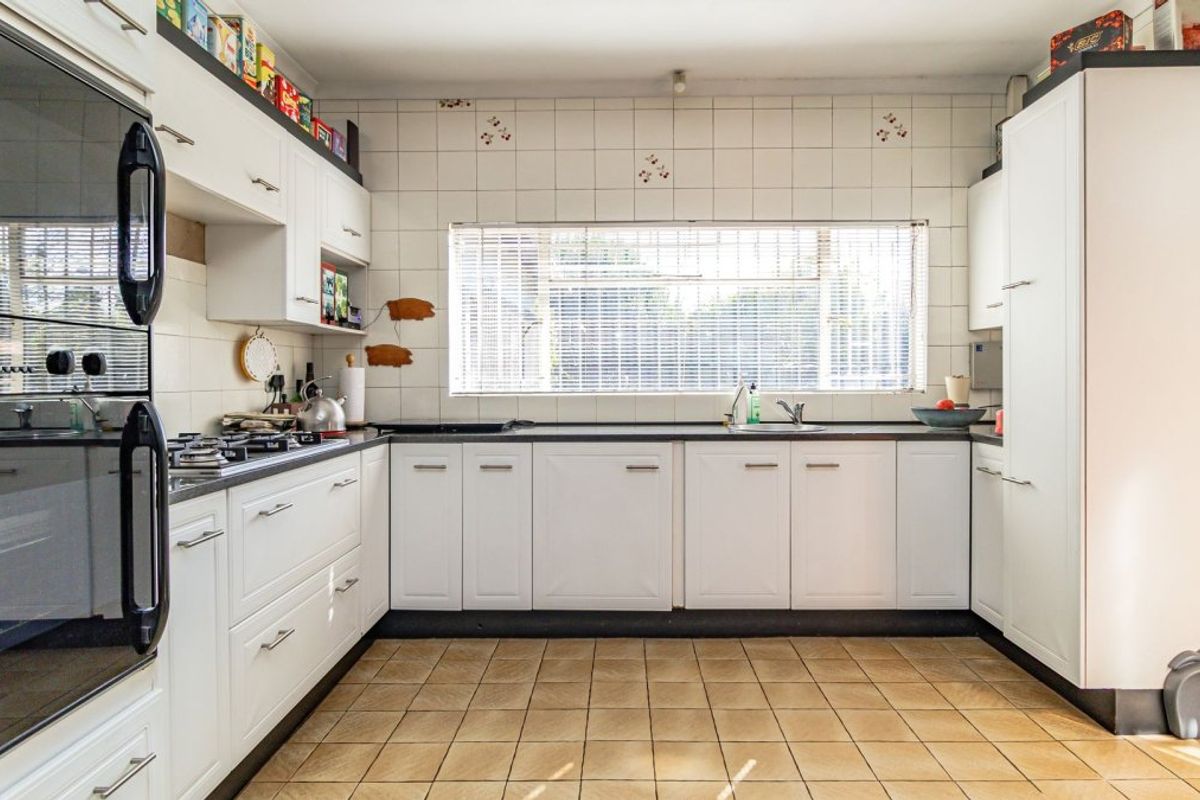Functional kitchen featuring white cabinetry, built-in oven, gas hob, and tiled splashback with a window overlooking the exterior.