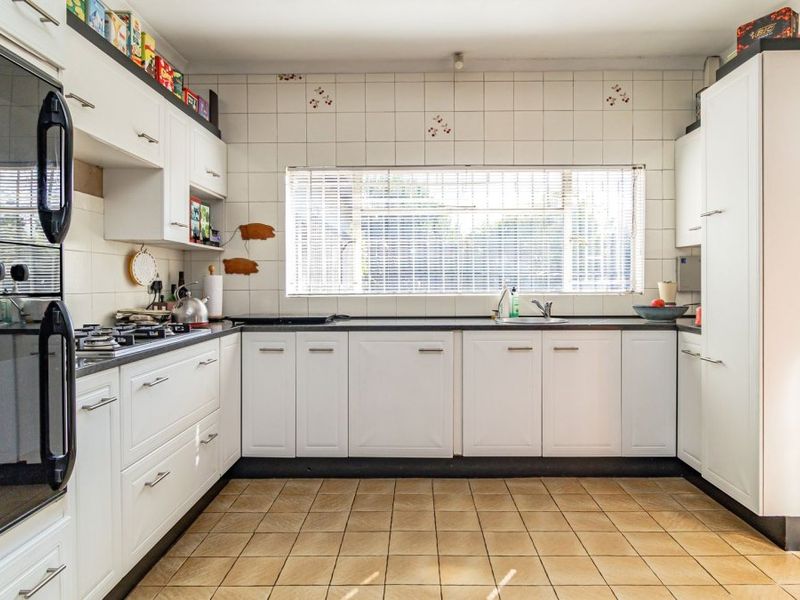Functional kitchen featuring white cabinetry, built-in oven, gas hob, and tiled splashback with a window overlooking the exterior.