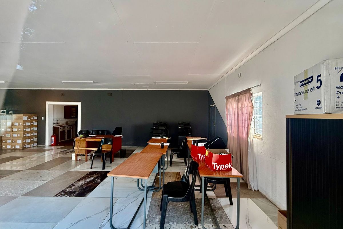 Spacious commercial office area featuring tiled flooring, fluorescent lighting, and access to an adjoining utility or kitchen space.