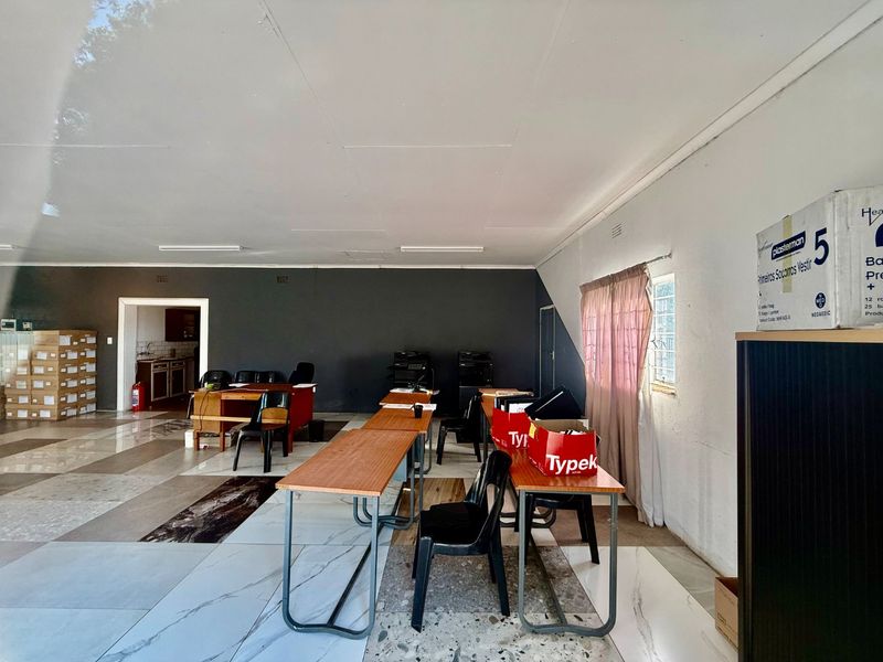 Spacious commercial office area featuring tiled flooring, fluorescent lighting, and access to an adjoining utility or kitchen space.