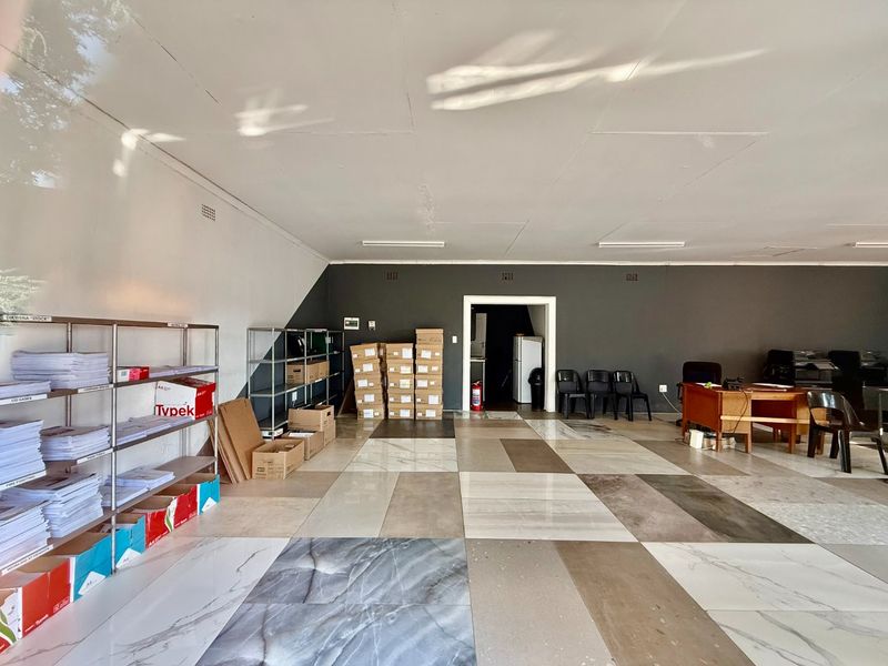 Spacious commercial office area featuring large format floor tiles, neutral wall finishes, and functional overhead lighting, suitable for various business operations.