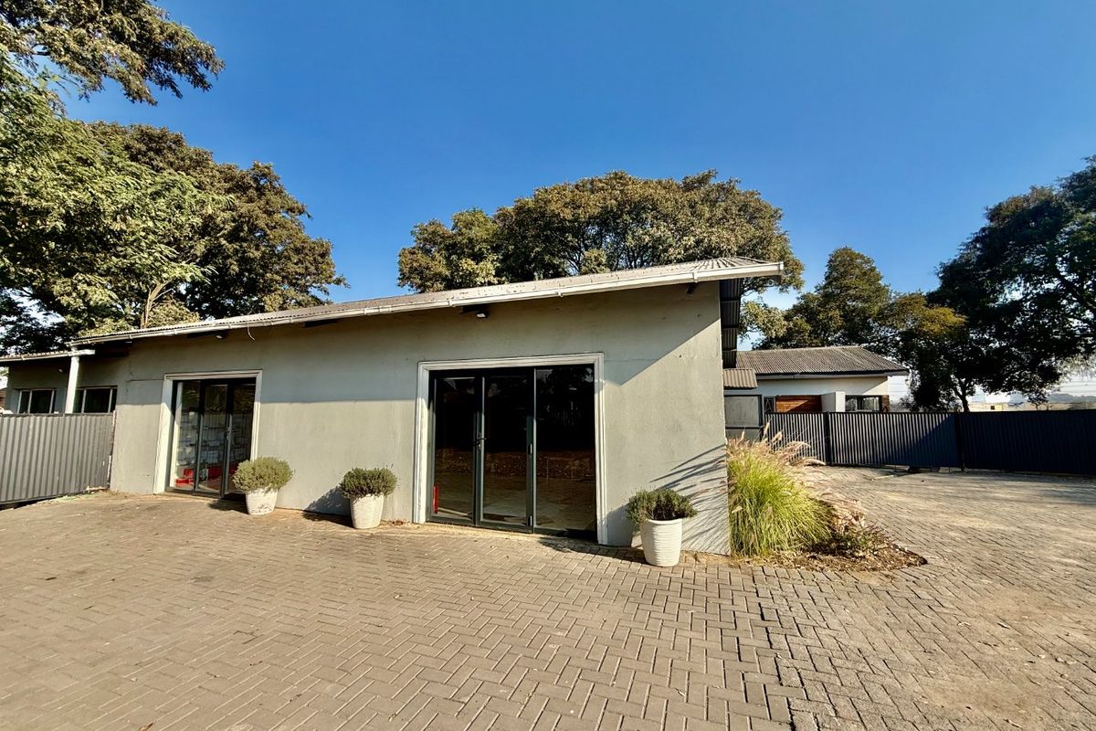 Front exterior view of a commercial building featuring a paved driveway, sliding glass doors, and metal roofing, set within a fenced property.