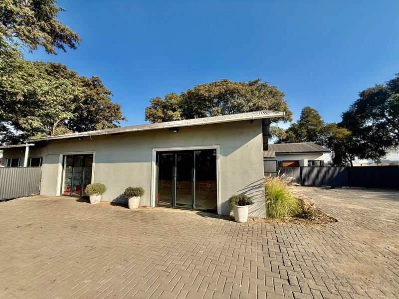 Front exterior view of a commercial building featuring a paved driveway, sliding glass doors, and metal roofing, set within a fenced property.