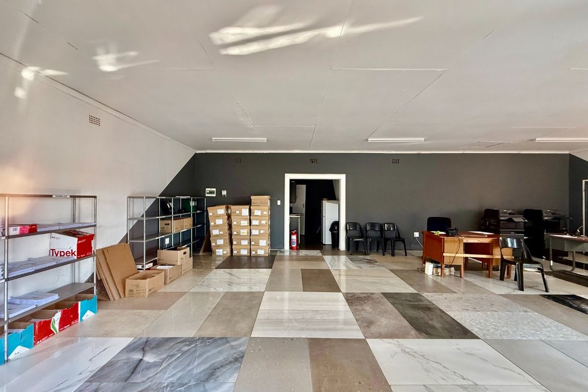 A spacious commercial office area featuring large format tiled flooring, neutral wall finishes, and overhead fluorescent lighting.