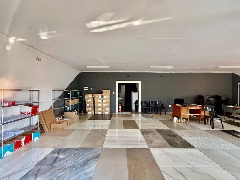 A spacious commercial office area featuring large format tiled flooring, neutral wall finishes, and overhead fluorescent lighting.
