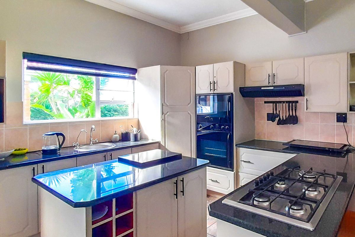 A functional kitchen featuring granite countertops, built-in cabinetry, a gas hob, an integrated oven, and a double sink with a garden-facing window.