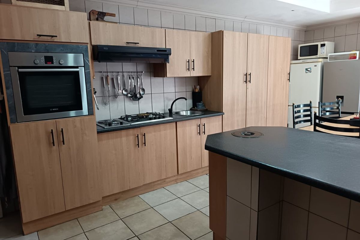 A functional kitchen featuring light wood cabinetry, a central island, tiled splashbacks, and built-in appliances including an oven and gas hob.