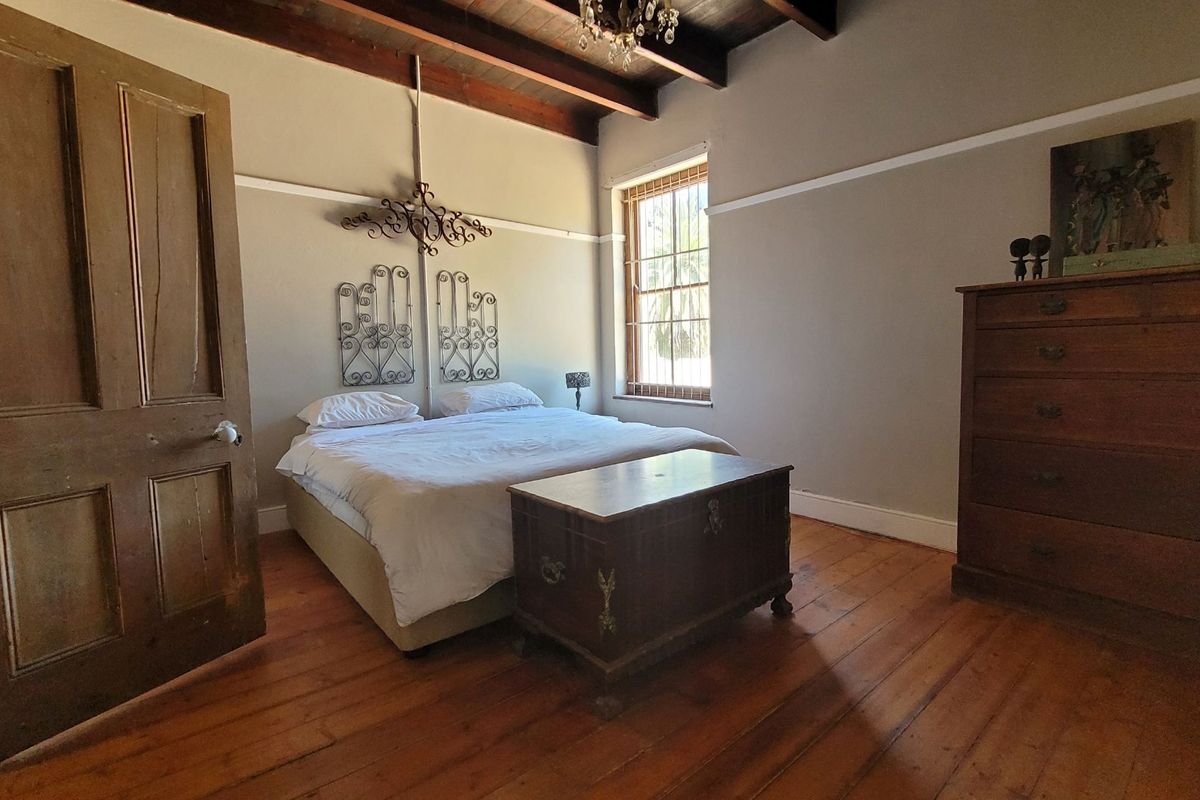 Spacious bedroom featuring original timber flooring, exposed wooden ceiling beams, and a classic sash window, offering a warm and character-filled living space.